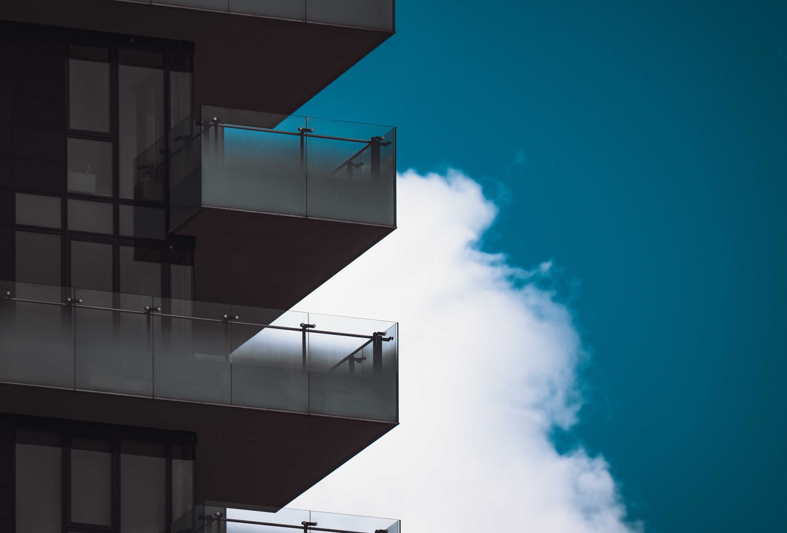 Modern building facade with glass balconies framed by a clear blue sky and white clouds.
